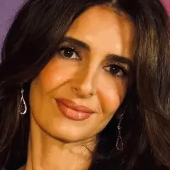 Amal Clooney, con su cabello oscuro y pendientes brillantes, sonríe ante la cámara.
