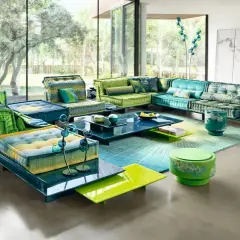 Un salón con sofás modulares en tonos verdes y azules, alfombra degradada y mesas de centro de cristal. Un look boho chic verano perfecto para relajarse.