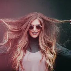 Chica sonriente con pelo largo y ondulado, mostrando cómo hidratar el pelo para un brillo radiante.