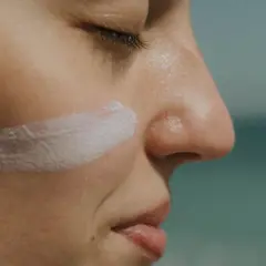 Aplicando crema solar biodegradable en la mejilla, protegiendo la piel del sol.