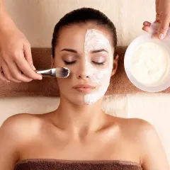 Una mujer recibe un tratamiento facial con una mascarilla aplicada con brocha.