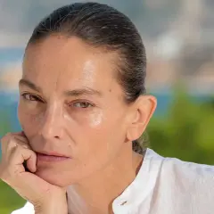 Retrato de **Laura Ponte joven**, con la mano apoyada en la barbilla, mirando pensativa. Fondo desenfocado de mar y vegetación.