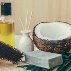 Aceite de coco para el pelo en botella junto a cocos partidos, jabón y cepillo.