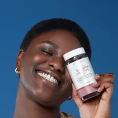 Mujer sonriente sostiene un frasco de gomitas de colágeno para la piel, con fondo azul.