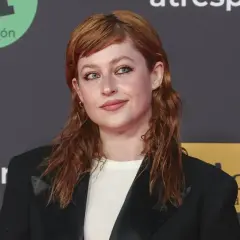 Chloe Wallace, con su cabello pelirrojo y mirada cautivadora, posa con un blazer negro.