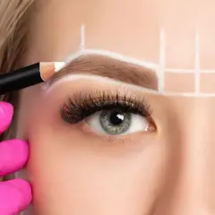 Manos enguantadas en rosa dibujan con lápiz blanco para crear cejas perfectas, marcando la simetría y el diseño.