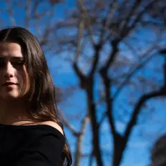 Elvira Lara, una joven con cabello castaño, mira a la cámara con un fondo de árboles y cielo azul.