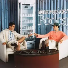 Los fundadores de Nude Project brindan con latas de su bebida, sentados en sillones frente a un cartel de neón del podcast de la marca.