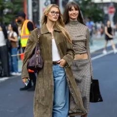 Dos mujeres pasean con un impecable estilo francés. Una lleva un abrigo largo verde oliva, vaqueros y un bolso de Dior. La otra luce un conjunto de cuadros con un top corto y falda.