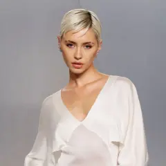 Iris Law, con su corte de pelo rubio platino y un elegante vestido blanco, posa con una mirada cautivadora.