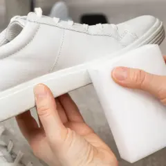 Manos limpiando zapatillas blancas piel con una esponja mágica. ¡Devolviendo el brillo a tus zapatos!