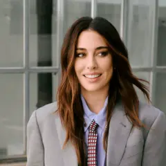 Blanca Suárez, con su melena castaña al viento, sonríe con confianza luciendo un traje gris y corbata.