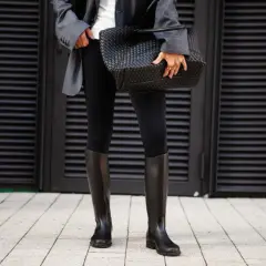 Elegante outfit con botas altas negras, chaqueta gris y bolso tejido.