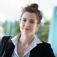Carlota Casiraghi sonríe con su cabello recogido en un moño, luciendo un blazer oscuro y un collar con un colgante en forma de corazón.