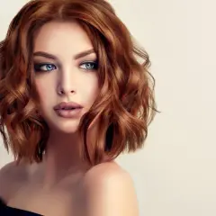 Mujer con cabello cobrizo ondulado en un elegante corte midi. Sus ojos azules y labios definidos resaltan su belleza.