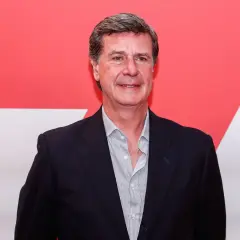 Javier Martínez de Irujo, con traje oscuro y camisa a rayas, sonríe ante un fondo rojo y blanco.