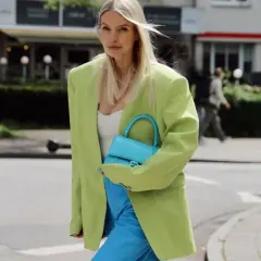 Mujer con blazer verde lima y pantalones azul eléctrico. Su bolso turquesa complementa perfectamente el conjunto, demostrando cómo el **verde y azul combinan** a la perfección.