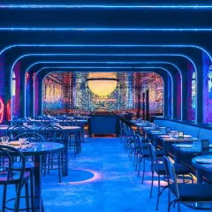 Un restaurante futurista con luces de neón azules y arte mural. Mesas puestas para cenar, quizás para disfrutar de una beata pasta bajo las estrellas.