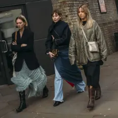 Tres mujeres caminan, mostrando que zapatos se llevan este invierno: botas altas negras, botines marrones y zapatos negros.