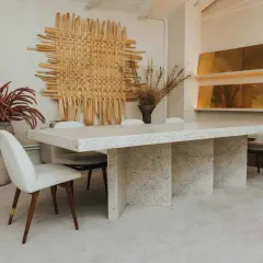 Comedor con mesa de terrazo y sillas tapizadas, arte de pared tejido y jarrones con flores secas. Un ambiente de lujo silencioso.