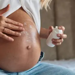 Manos aplicando crema en el vientre de una mujer embarazada. La crema, con un toque de rosa mosqueta, ayuda a cuidar la piel.