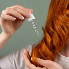Manos aplicando aceite en cabello pelirrojo. El hair oiling nutre y da brillo.
