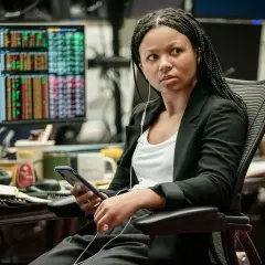 Myha'la Herrold, con auriculares, revisa su teléfono en una oficina con pantallas de datos financieros.
