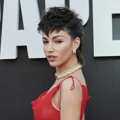 Mujer con un llamativo mullet corto, maquillaje rojo y vestido rojo, luciendo un collar de perlas.