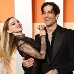La pareja Dove Cameron y Dylan Sprouse ríen juntos, ella con un vestido de encaje negro y él con un traje negro.
