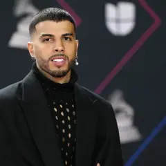 Rauw Alejandro, de Puerto Rico, posa con un traje negro y un suéter de red.