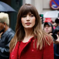 Mujer con flequillo y cabello castaño ondulado, luciendo un abrigo rojo. Un adelanto de los cortes de pelo 2026 mujer.
