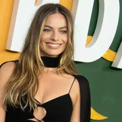 Margot Robbie sonríe con un vestido negro. La pregunta de cuanto mide Margot Robbie es un misterio, pero su estilo es innegable.