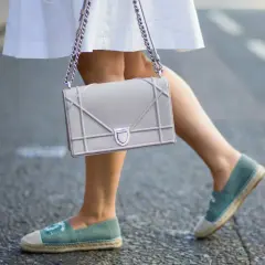 Piernas con un outfit veraniego, falda blanca y un bolso gris, completado con unas cómodas alpargatas de tela azul.