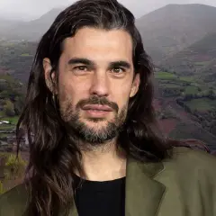 Oliver Laxe, director, posa con una barba cuidada y pelo largo, frente a un paisaje montañoso de Galicia.