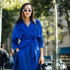 Mujer con gabardina azul eléctrico, gafas blancas y bolso negro, paseando por la calle.