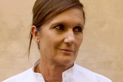Retrato de Maria Grazia Chiuri, diseñadora de moda, con un collar dorado y camisa blanca.