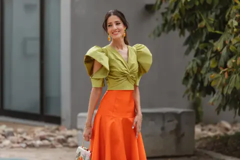 Elegante look invitada boda otoño: top verde con volantes y falda naranja.