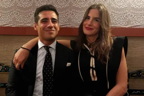 Pareja sonriente, él con traje y corbata de puntos, ella con vestido negro. Blanca Llandres, un momento íntimo capturado.