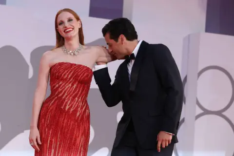 Oscar Isaac besa la mano de Jessica Chastain, quien luce un vestido rojo brillante y un collar de diamantes.