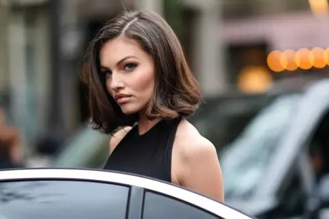 Mujer con corte bob asimétrico, ideal para cortes de pelo para cara redonda, luciendo elegante junto a un coche.
