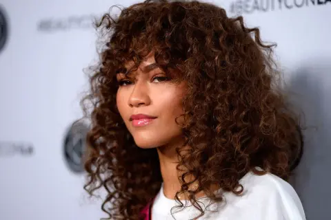 Mujer con pelo muy corto rizado natural, castaño y voluminoso, con flequillo.