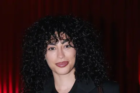 Mina El Hammani, con su cabello rizado y oscuro, sonríe ante un fondo de cortinas rojas.