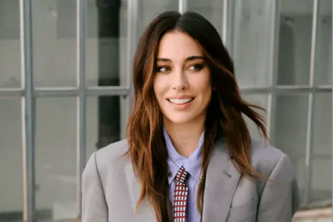 Blanca Suárez, con su melena castaña al viento, sonríe con confianza luciendo un traje gris y corbata.