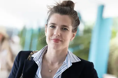 Carlota Casiraghi sonríe con su cabello recogido en un moño, luciendo un blazer oscuro y un collar con un colgante en forma de corazón.