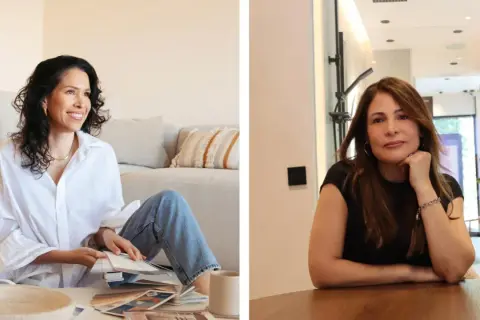 Veronica Blume, diseñadora, revisa muestras de color en el suelo junto a un sofá. A su lado, otra mujer sonríe apoyada en una mesa.