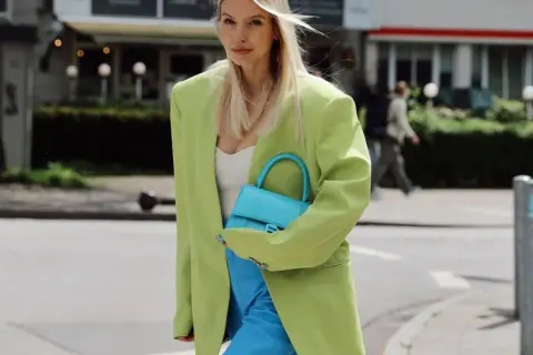 Mujer con blazer verde lima y pantalones azul eléctrico. Su bolso turquesa complementa perfectamente el conjunto, demostrando cómo el **verde y azul combinan** a la perfección.