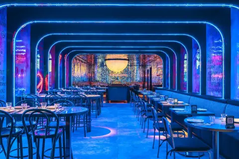 Un restaurante futurista con luces de neón azules y arte mural. Mesas puestas para cenar, quizás para disfrutar de una beata pasta bajo las estrellas.