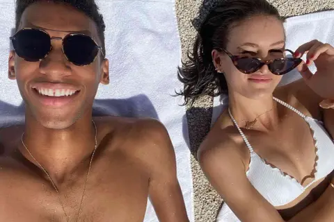 Felix Auger-Aliassime y su novia disfrutan del sol en la playa. Él sonríe a la cámara, ella se ajusta las gafas de sol.