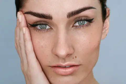 Rostro de mujer con microblading cejas perfectas, delineado de ojos y piel con pecas.