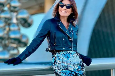 Mujer sonríe con gafas de sol, chaqueta de cuero y falda de lentejuelas azul brillante. ¡Un look audaz para combinar falda lentejuelas!